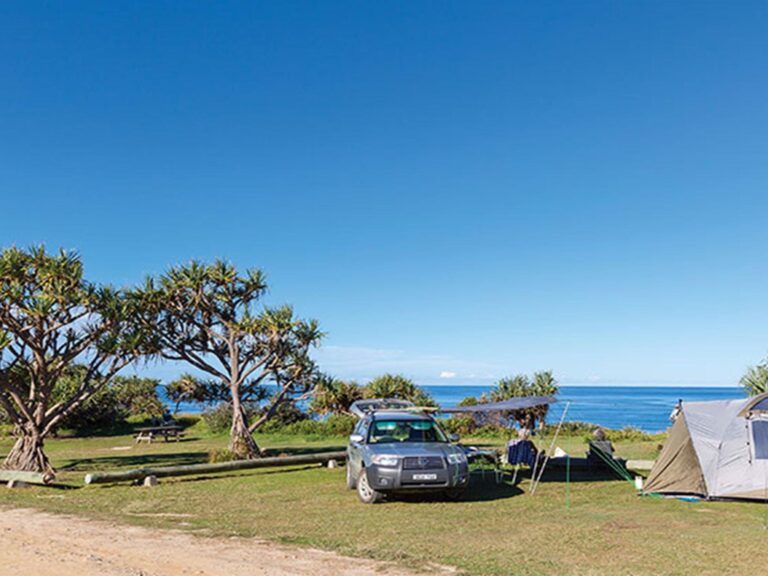 A tent pitched next to a car with the beach in the background at Red Cliff campground in Yuraygir