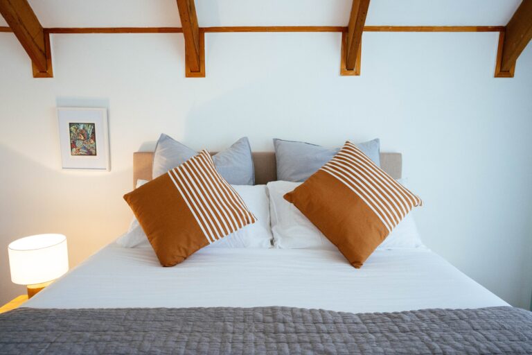 A queen sized bed with white linen and orange and light blue pillows